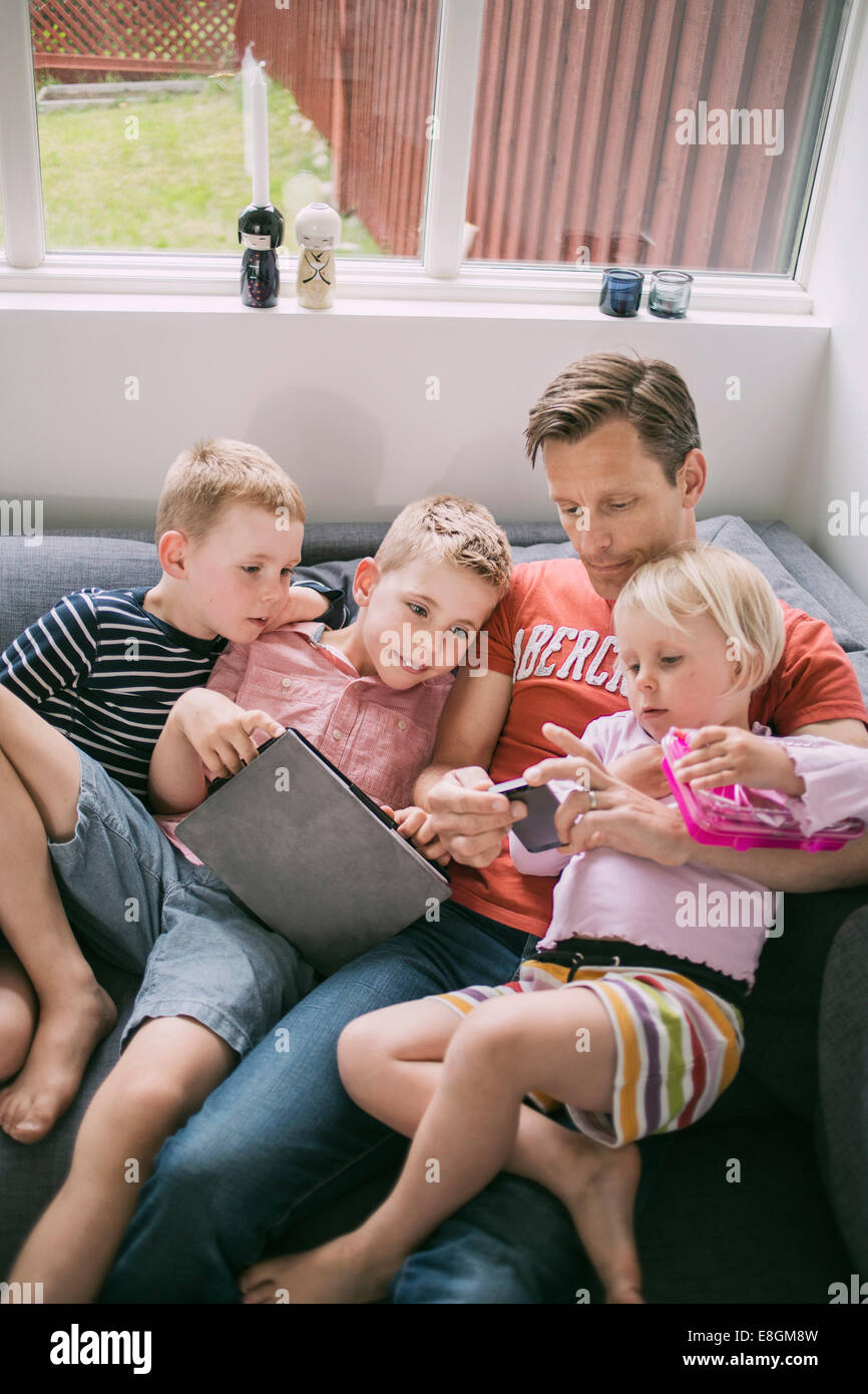 Father and children using technologies on sofa at home Stock Photo