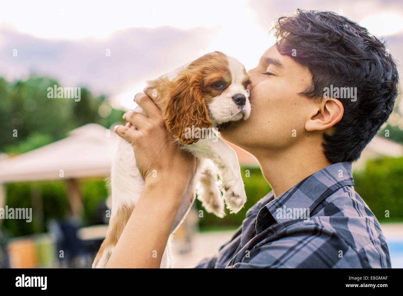 Side view of young man kissing dog in yard Stock Photo