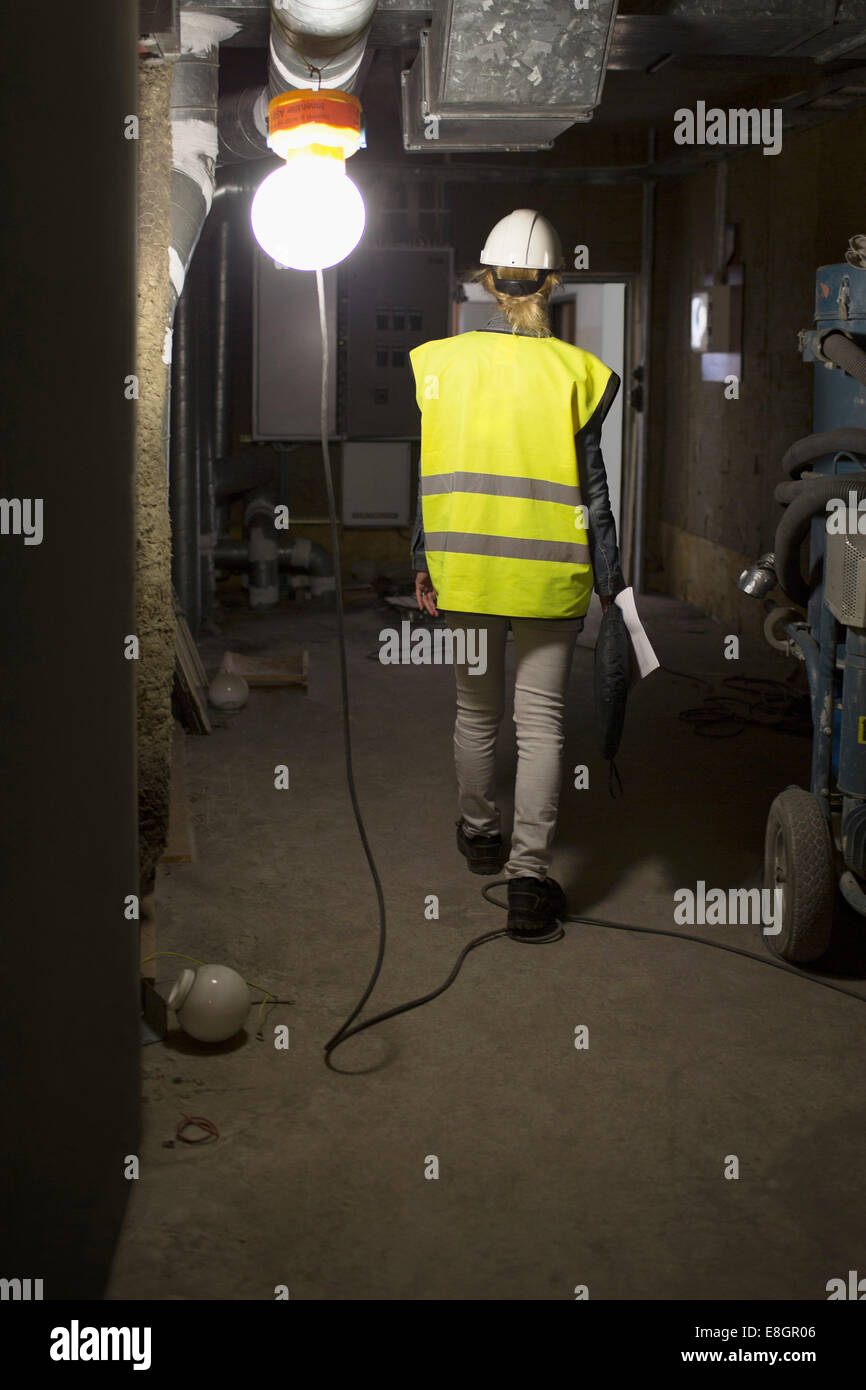 Full length rear view of female construction worker walking in illuminated room Stock Photo