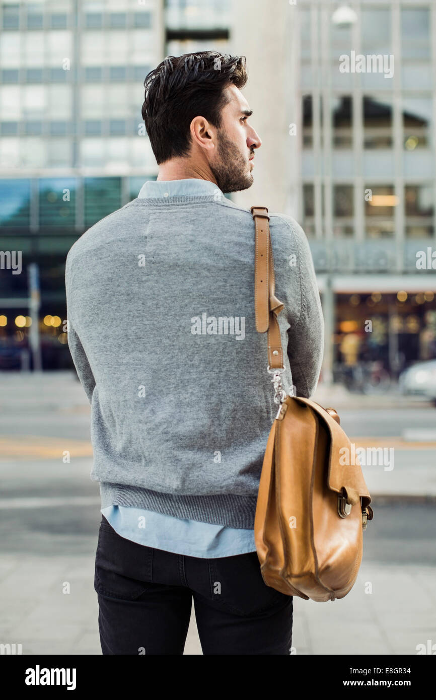 Rear view of businessman carrying shoulder bag on city street Stock