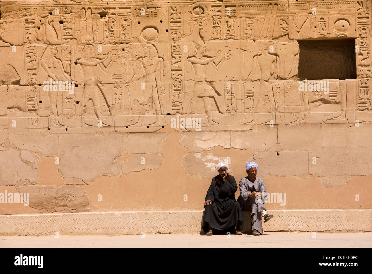 Egypt, Luxor, Karnak Temple, two local guides sat below bas reliefs and hieroglyphics Stock Photo