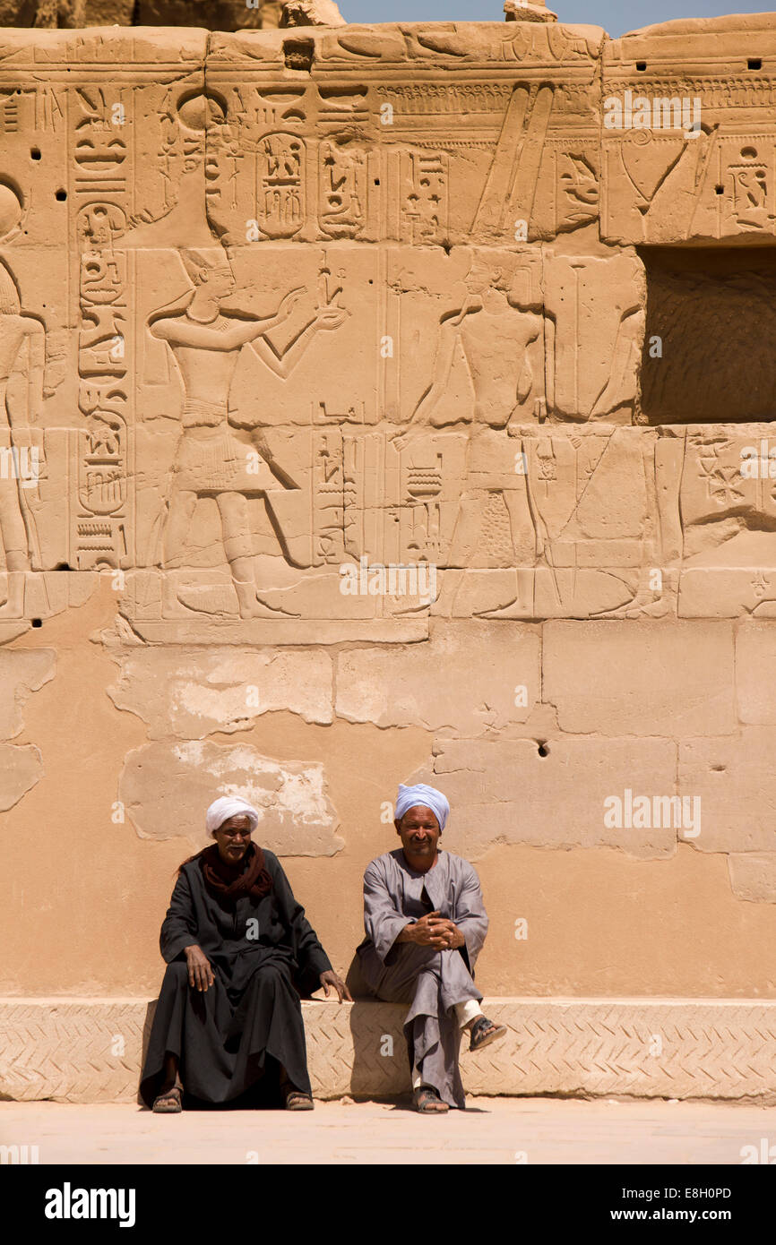 Egypt, Luxor, Karnak Temple, two local guides sat below bas reliefs and hieroglyphics Stock Photo
