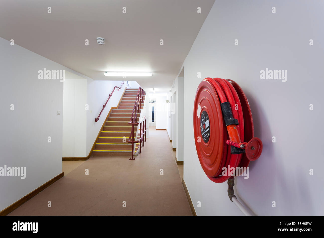 Fire hose on wall inside building by staircase. Stock Photo