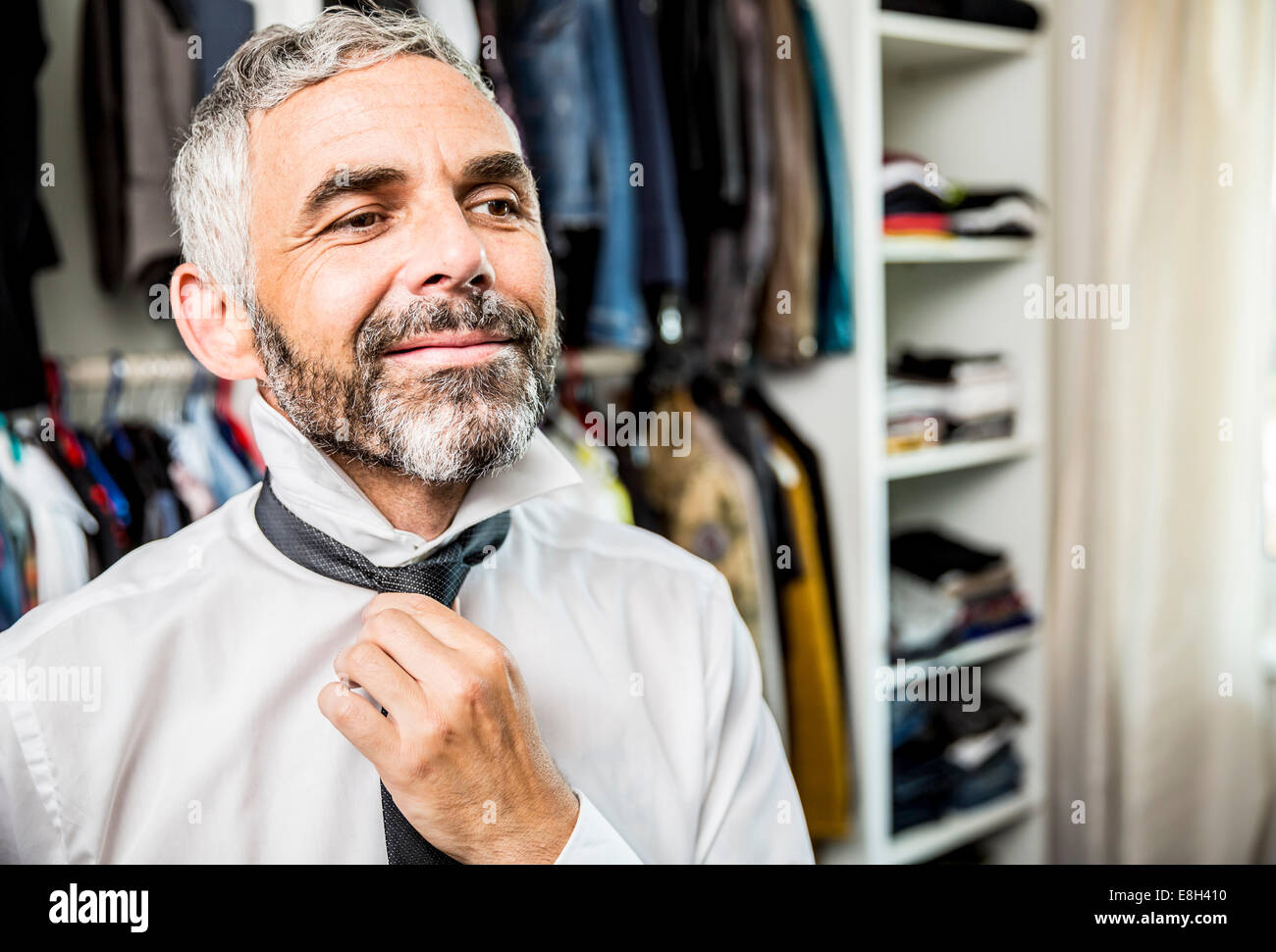 Portrait of smiling businessman binding tie at his walk-in closet Stock Photo