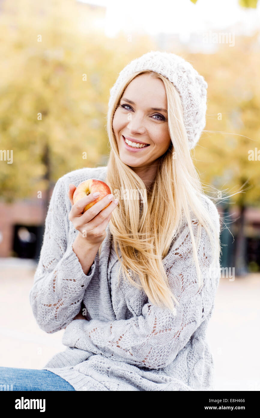 Portrait of smiling young woman holding an apple wearing wooly hat and ...