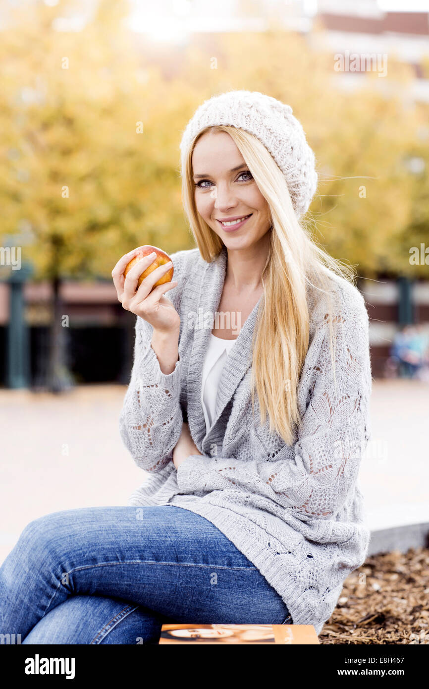 Portrait of smiling young woman holding an apple wearing wooly hat and ...