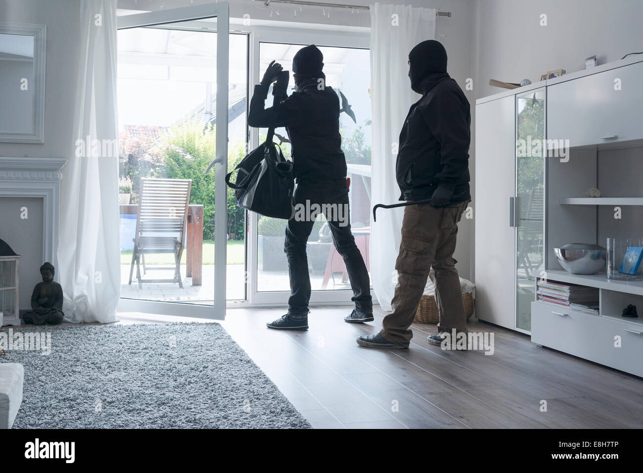Two burglars leaving an one-family house with their loot at daytime Stock Photo