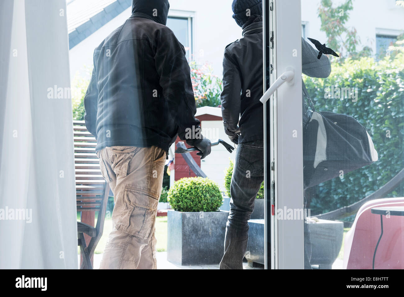Two burglars leaving an one-family house with their loot at daytime Stock Photo