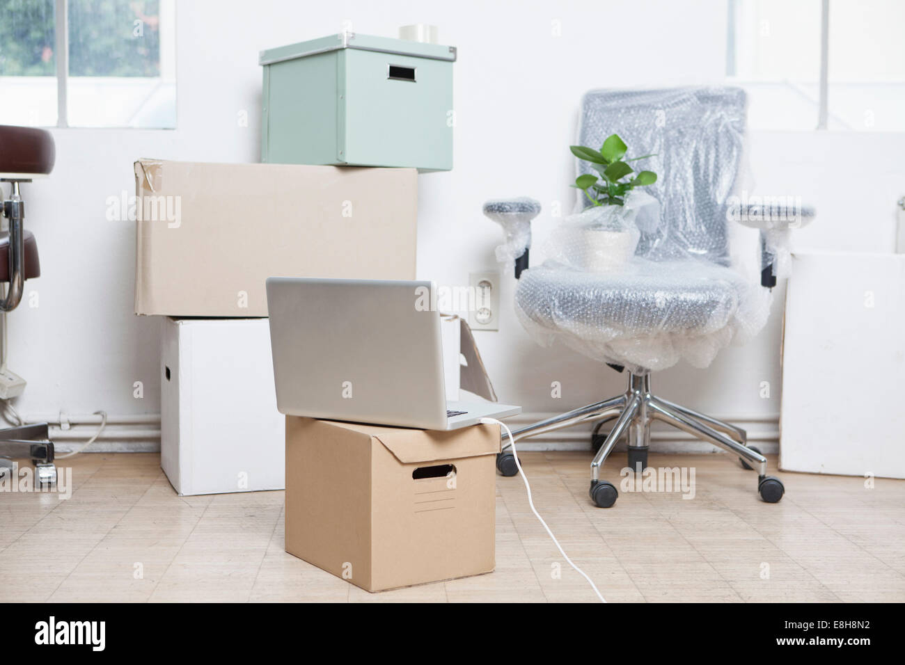Stack of cardboard boxes, wrapped swivel chair and a notebook in an office Stock Photo