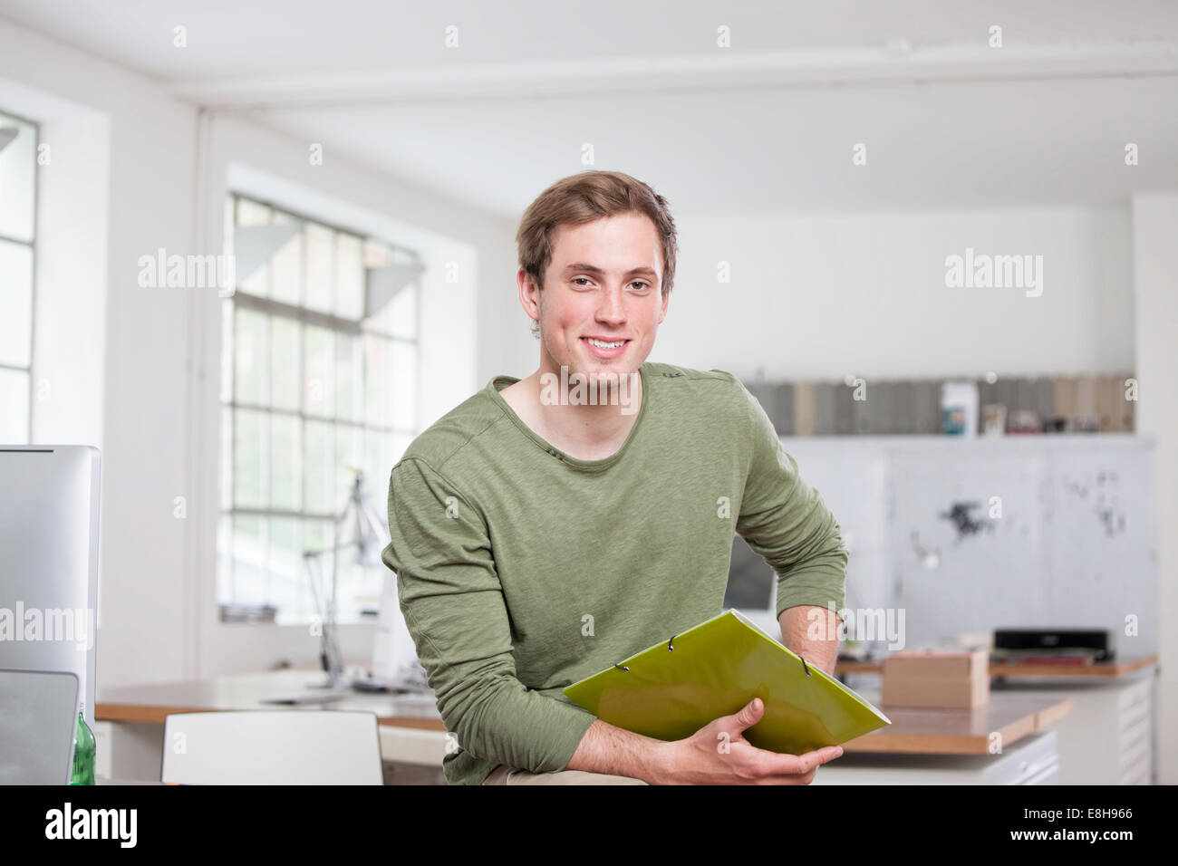 Portrait of smiling young man sitting on his desk in the office Stock ...