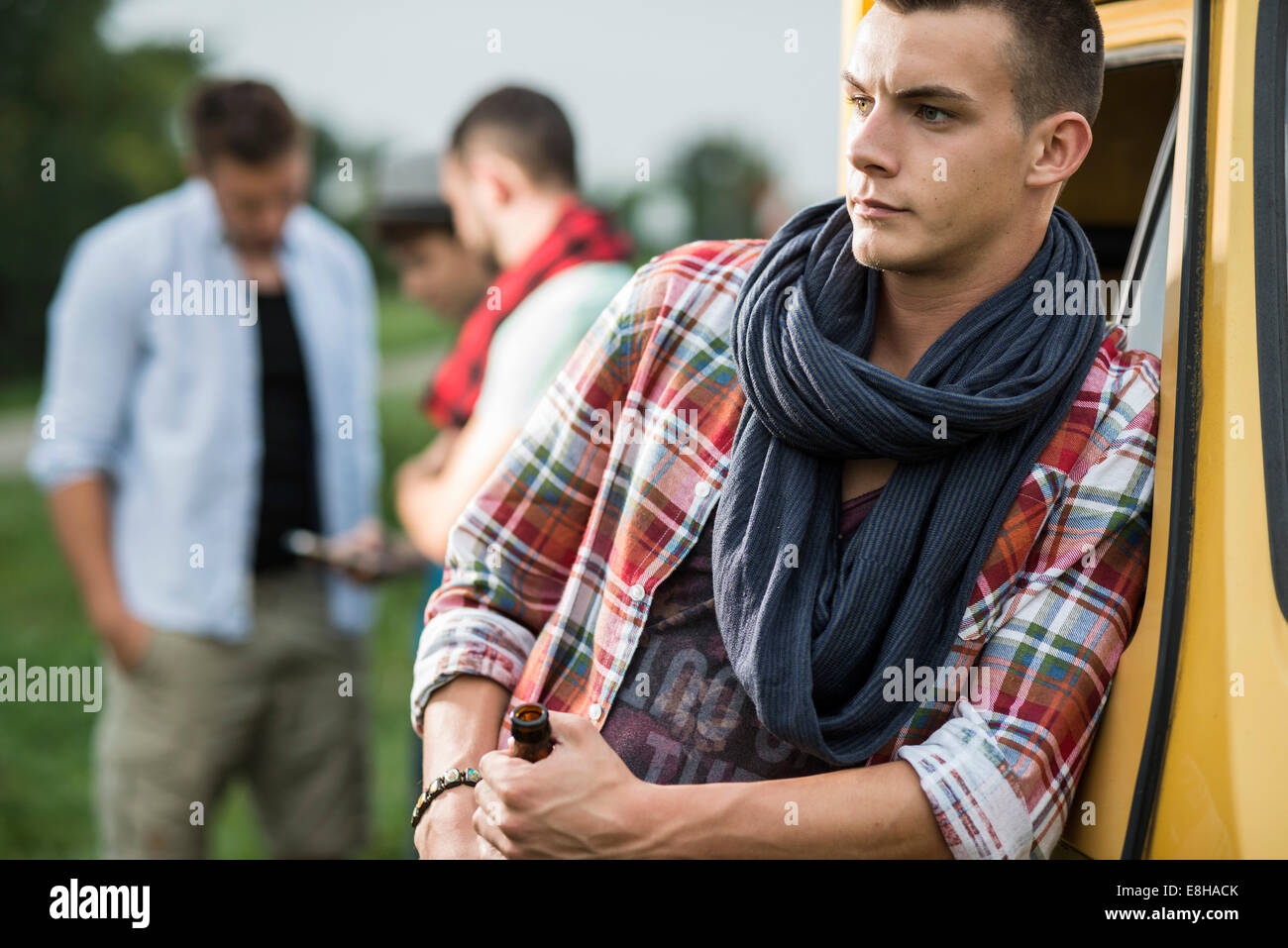 Young man holding bottle of beer leaning against vehicle Stock Photo