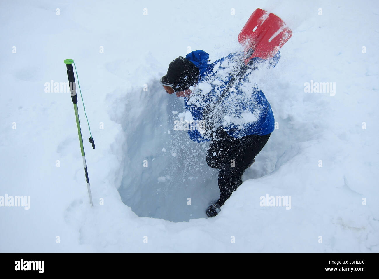 Man digging his way towards victim marked by a snow probe. Avalanche rescue training. Stock Photo