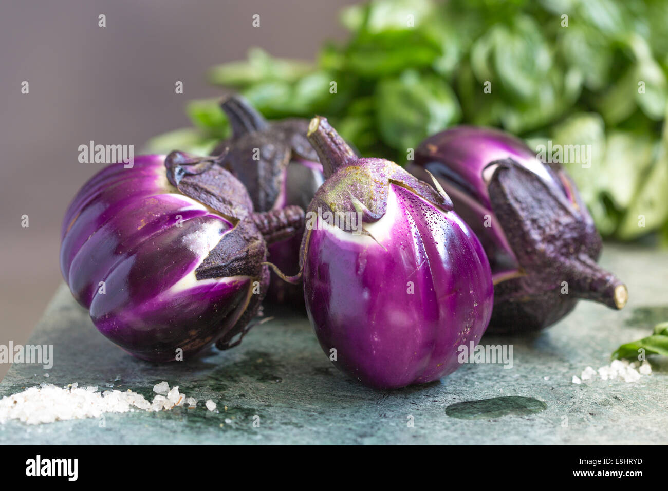 group of aubergines on green marble, with salt foreground and basil in the background. Stock Photo