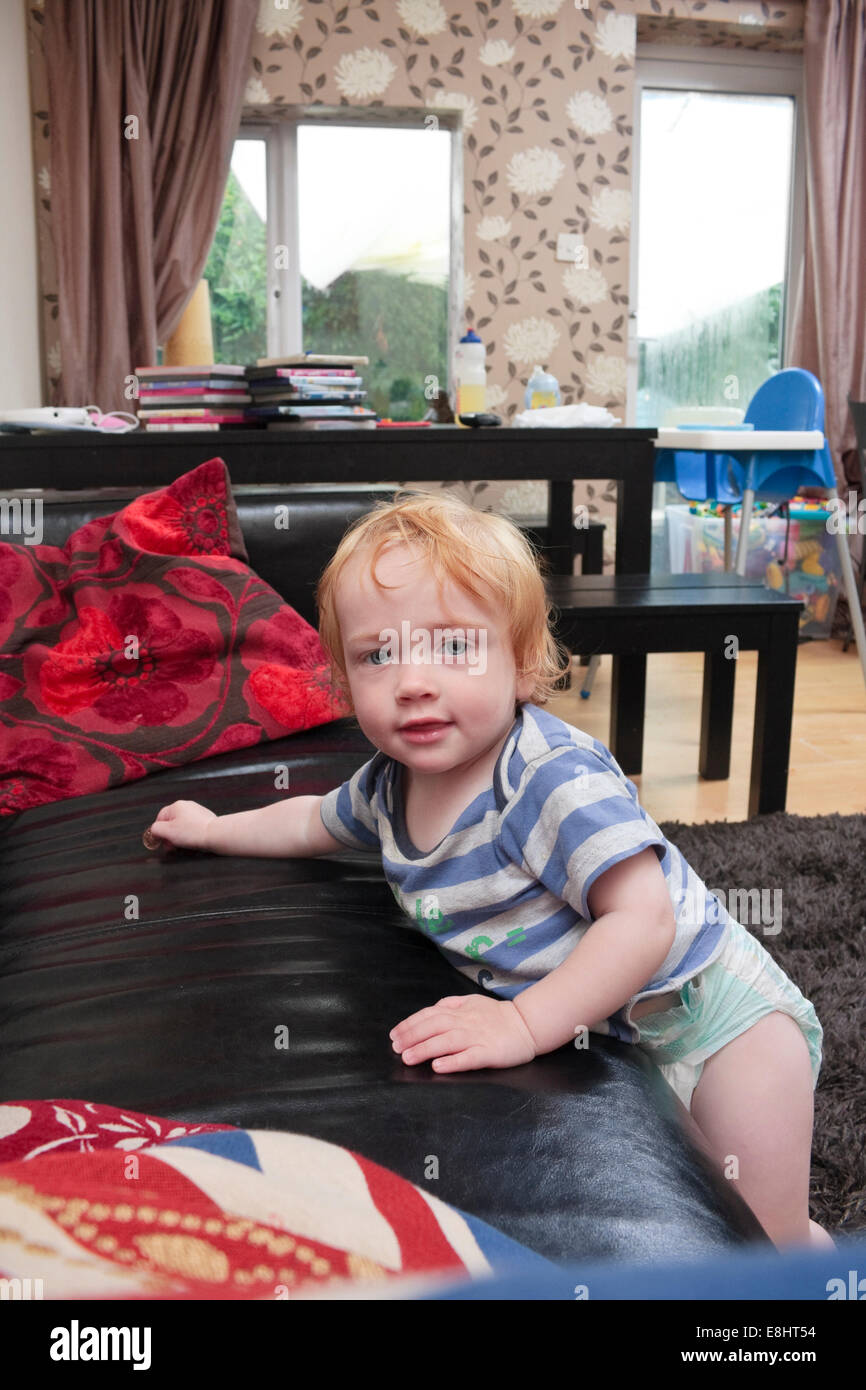 A oneyear old boy attempting to climb up on a black sofa in a home living room Stock Photo Alamy