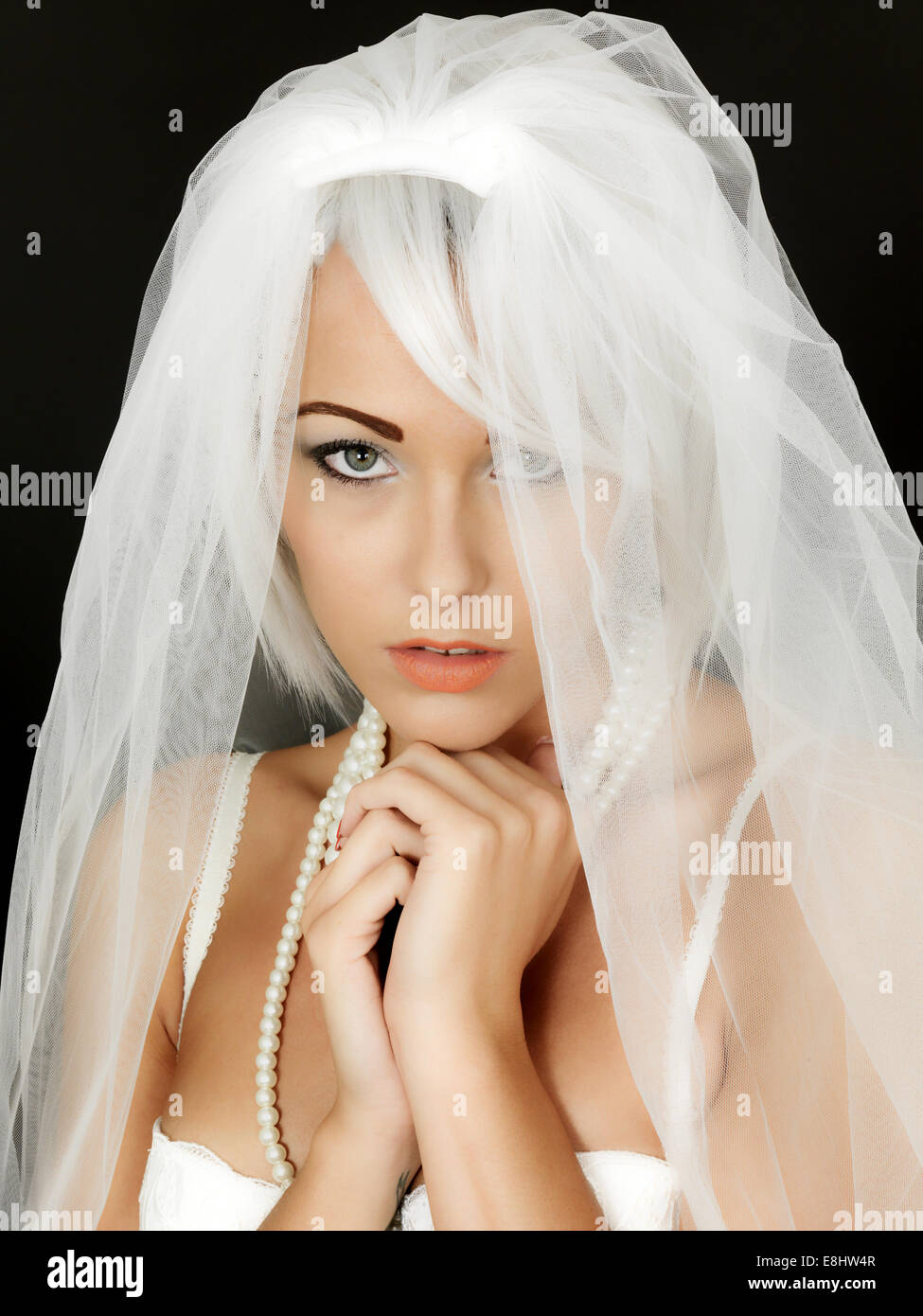 Young Woman Bride To Be Wearing A White Wedding Veil Anticipating A New Life And Beginning In A Life Partnership Isolated Against A Black Background Stock Photo