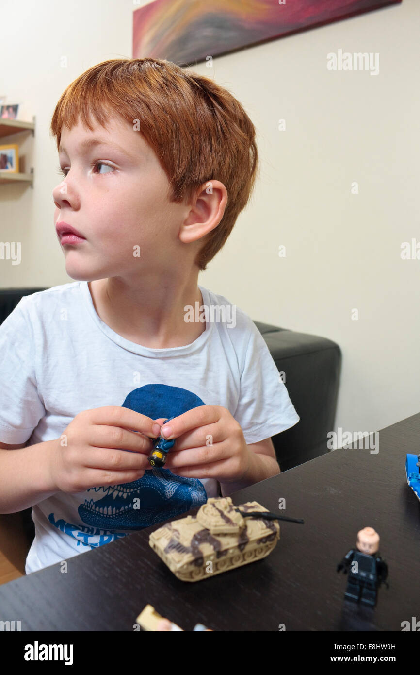 A five year old boy playing with small toys at the dinner table in a