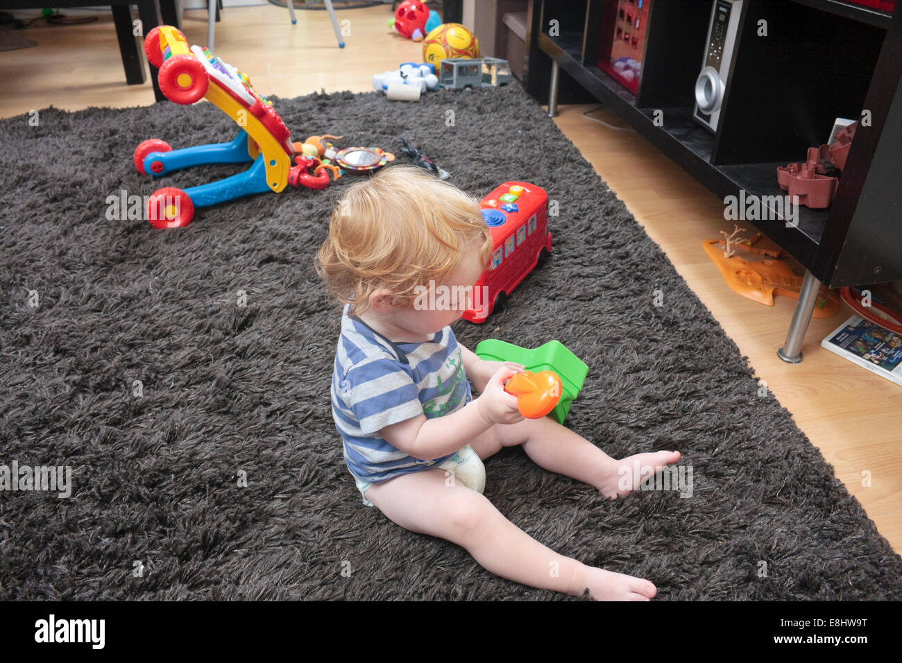 A one-year old boy playing with toys on a carpet in a living room setting Stock Photo