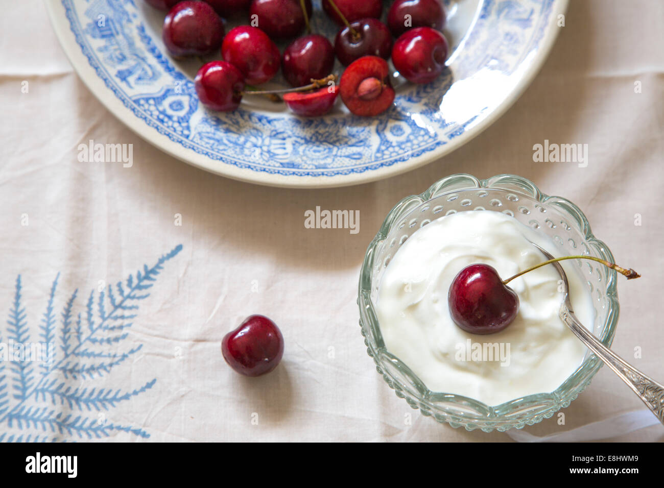 whole cherries on blue ceramic plate, on leaf linen and cream or yogurt in glass dish Stock Photo