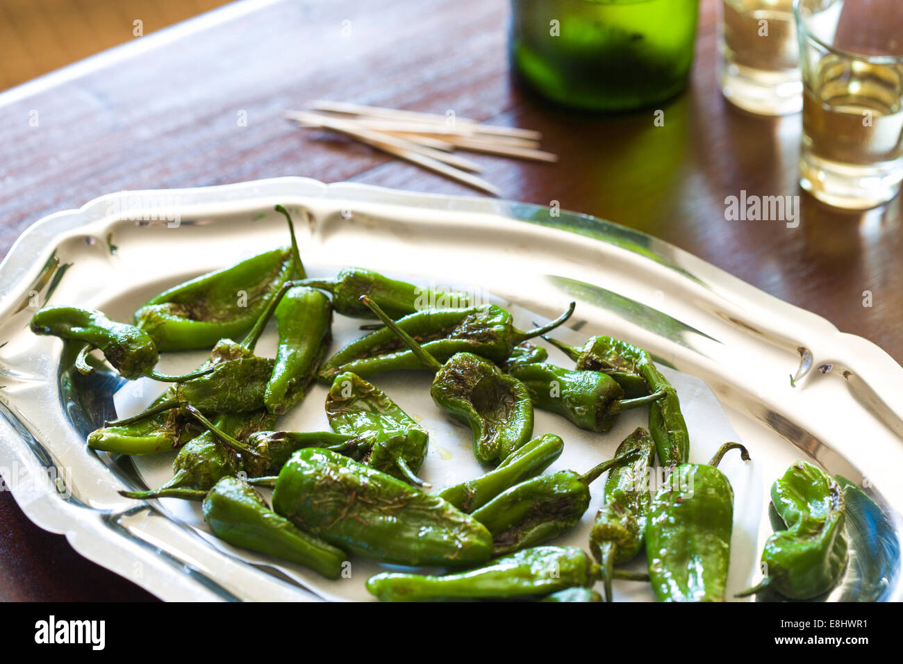 padron peppers as a typical Spanish tapas style snack on wood table , with sherry glasses and bottle in background Stock Photo