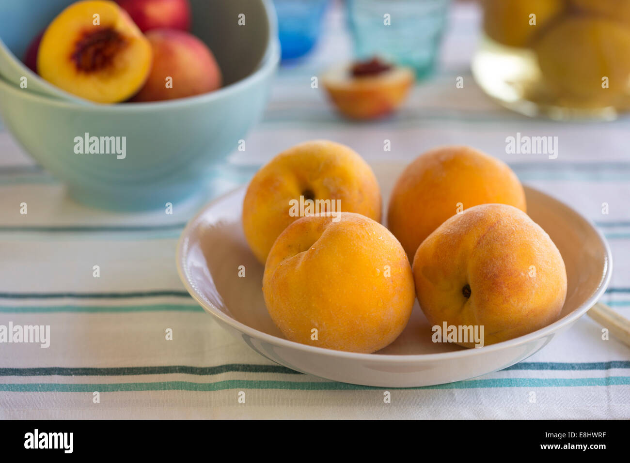 summer picnic of yellow peaches in a dish, with aqua bowls of nectarines and preserved peaches in background Stock Photo