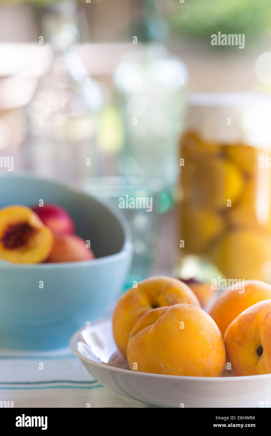 summer picnic of yellow peaches in a dish, with aqua bowls of nectarines and preserved peaches in background Stock Photo