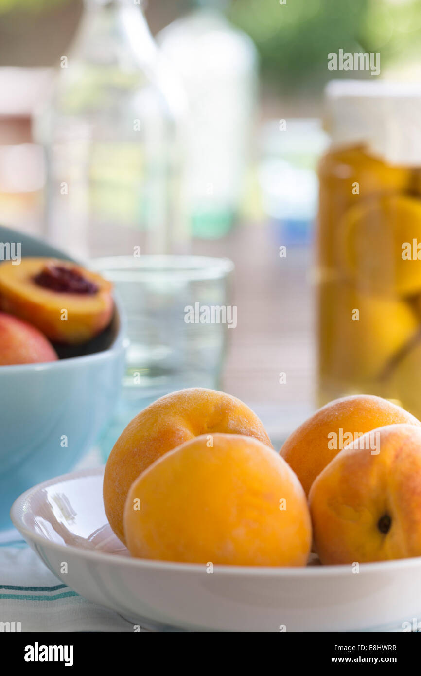 summer picnic of yellow peaches in a dish, with aqua bowls of nectarines and preserved peaches in background Stock Photo