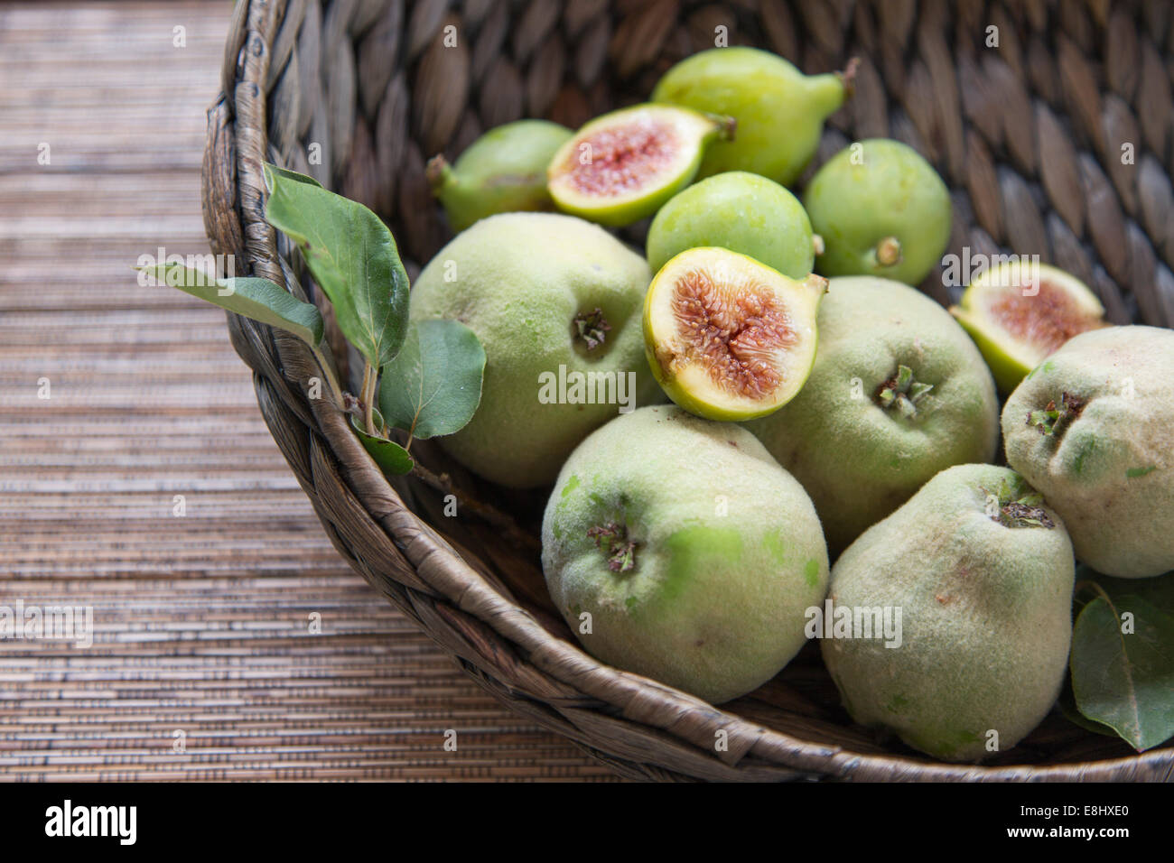 quinces and figs in woven basket with cut figs on top Stock Photo