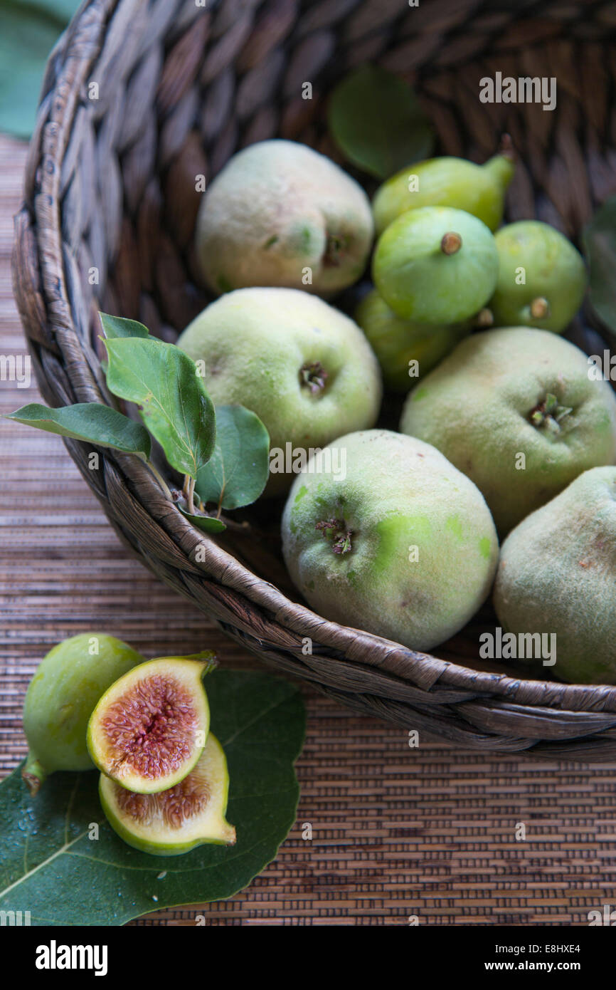 quinces and figs in woven basket with cut figs in foreground Stock Photo