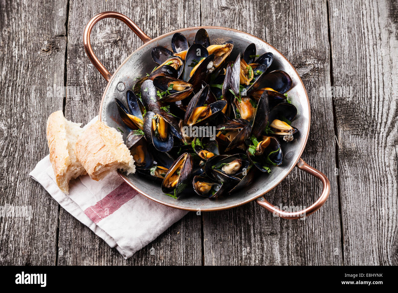 Mussels in copper cooking dish and French Baguette on dark wooden background Stock Photo