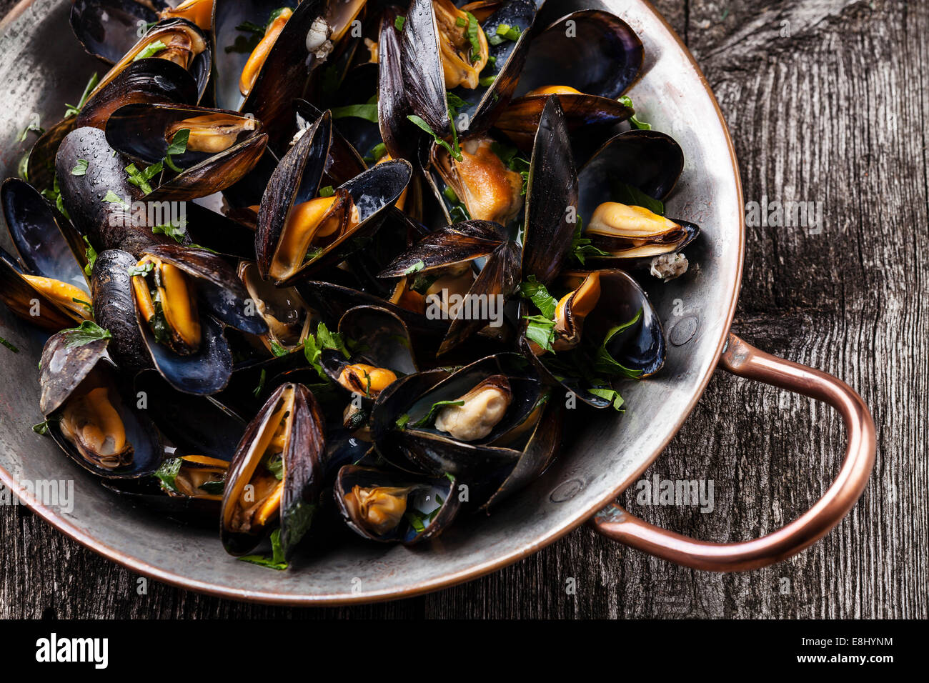 Boiled mussels in copper cooking dish on dark wooden background close up Stock Photo