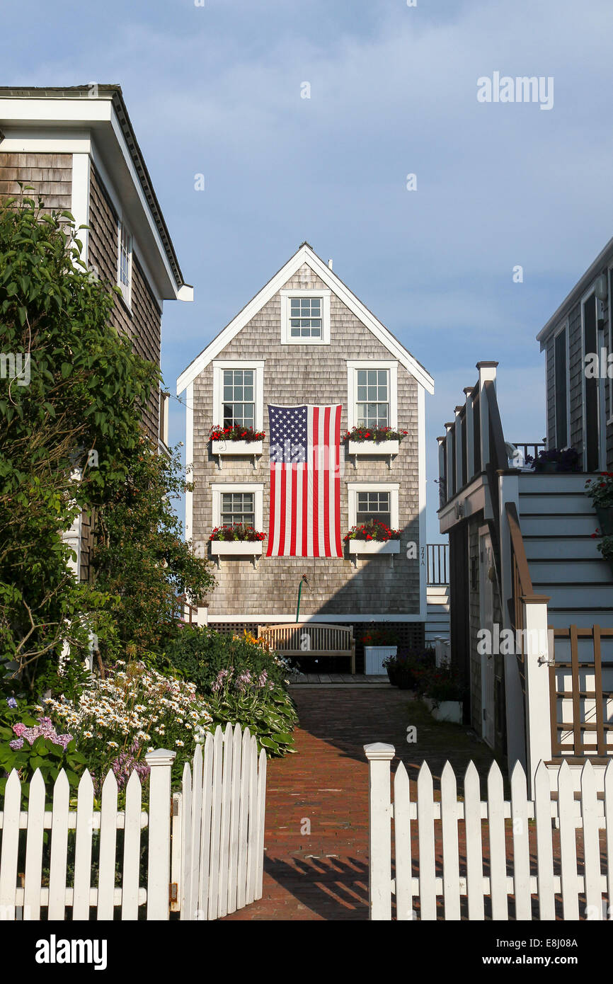 A gate opens towards a pretty house with flower boxes on   windows, draped with a large American flag. Provincetown, Cape Cod Stock Photo