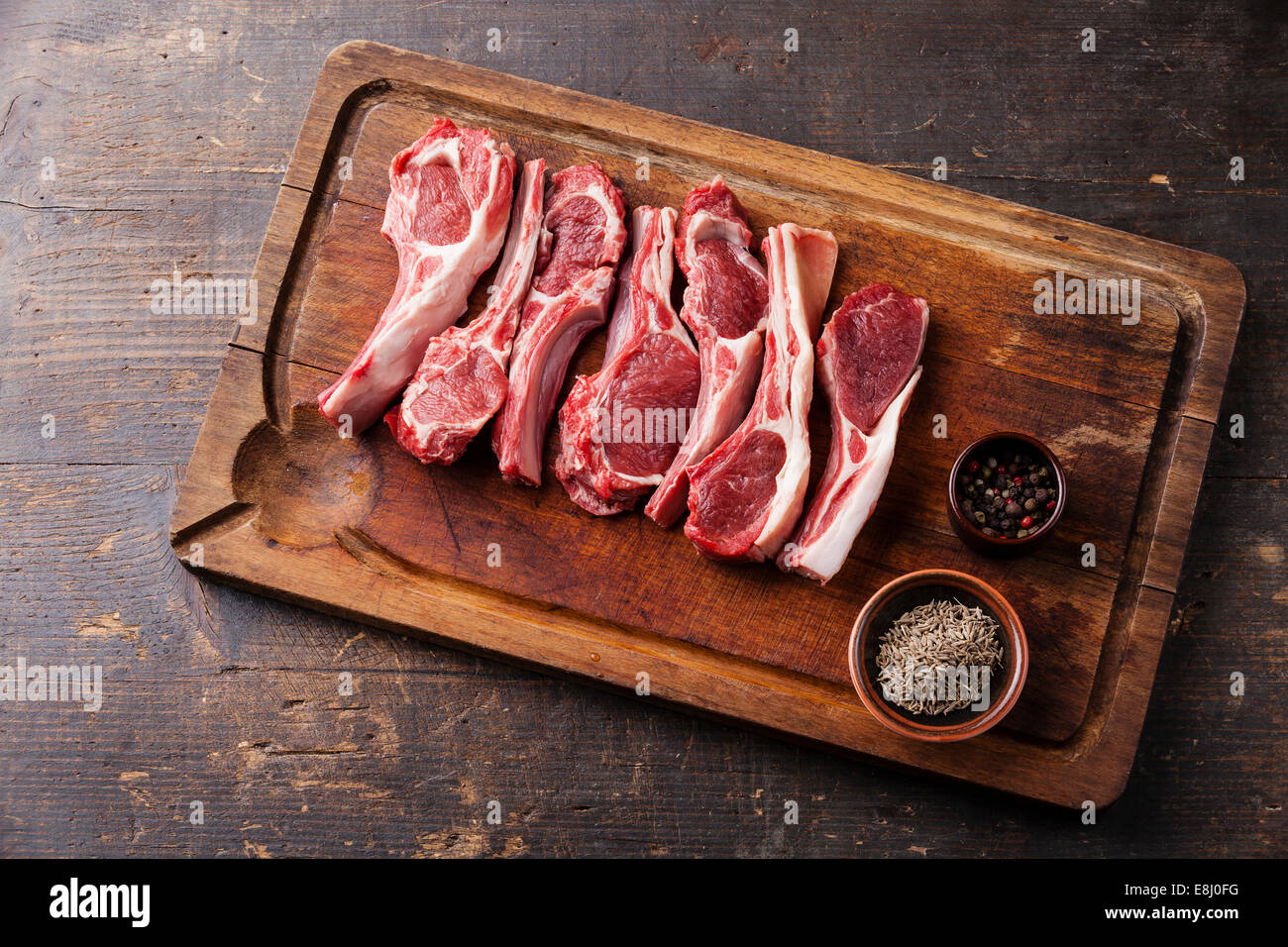 Raw fresh lamb ribs with pepper and cumin on wooden cutting board on dark background Stock Photo