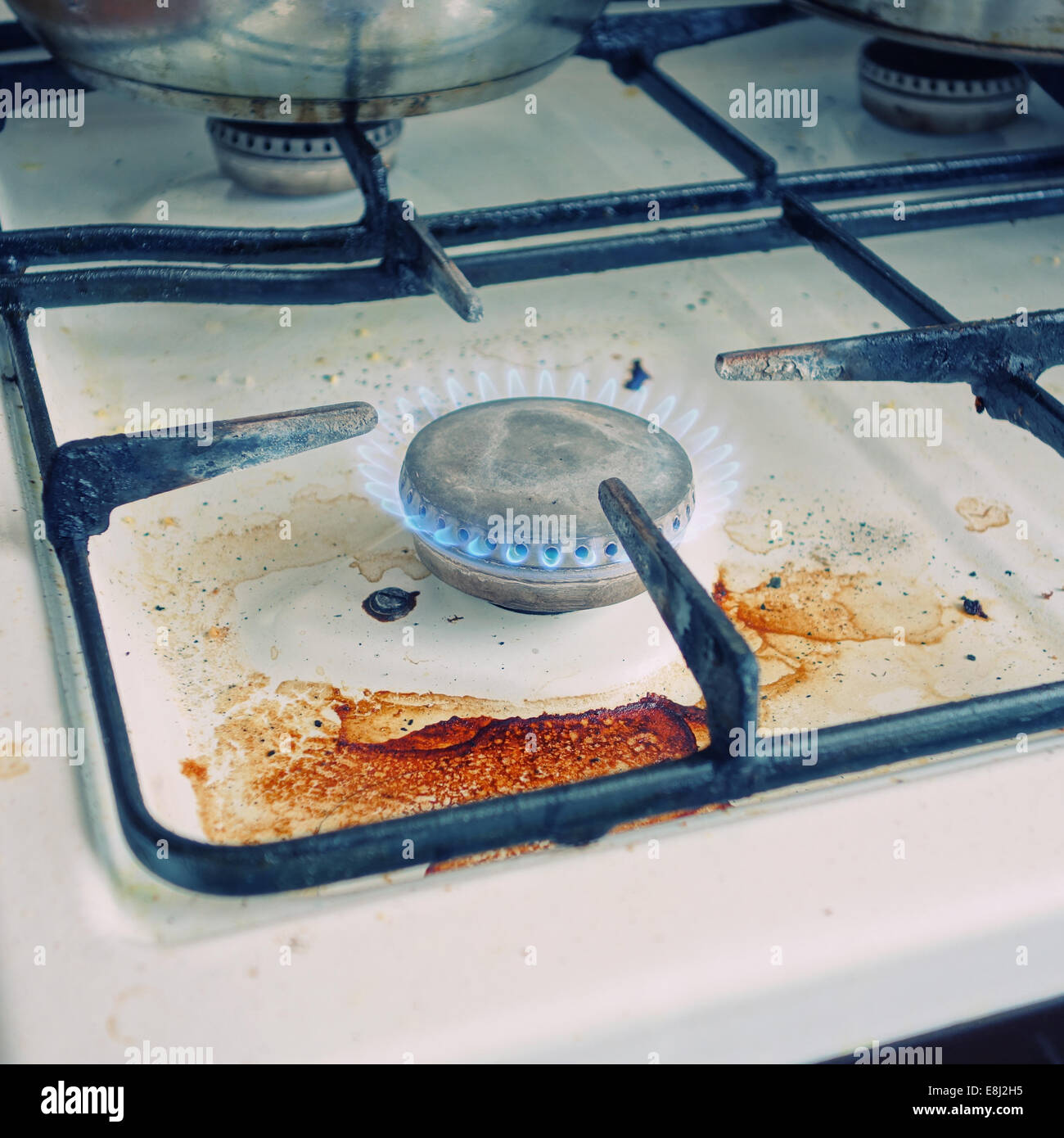 Old dirty gas cooker with flame burning. Cross-processed. Stock Photo