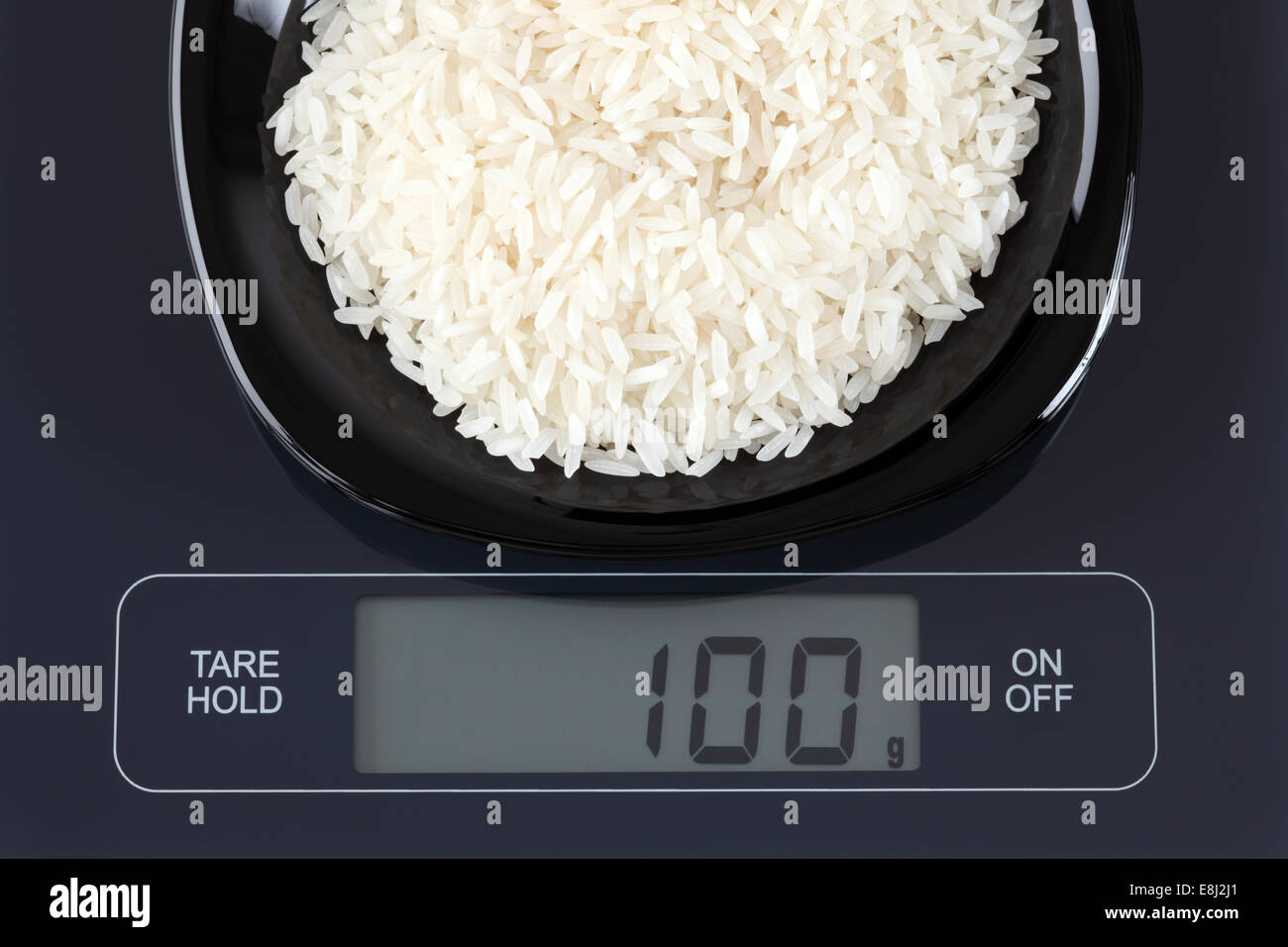 White rice in a black plate on digital scale displaying 100 gram ...