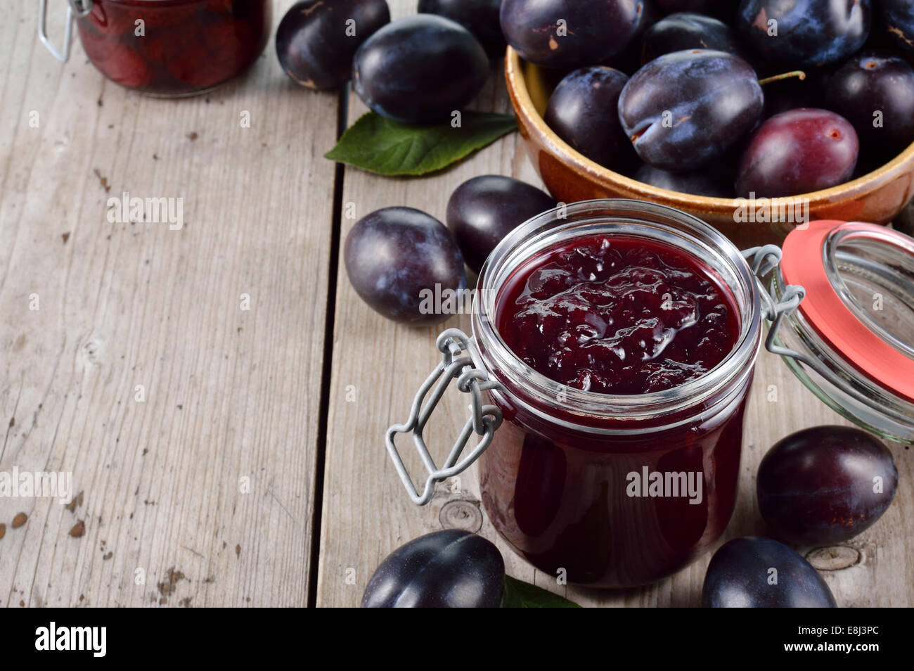 Homemade plum jam and group of plums on old wooden table. Plenty of copyspace. Stock Photo