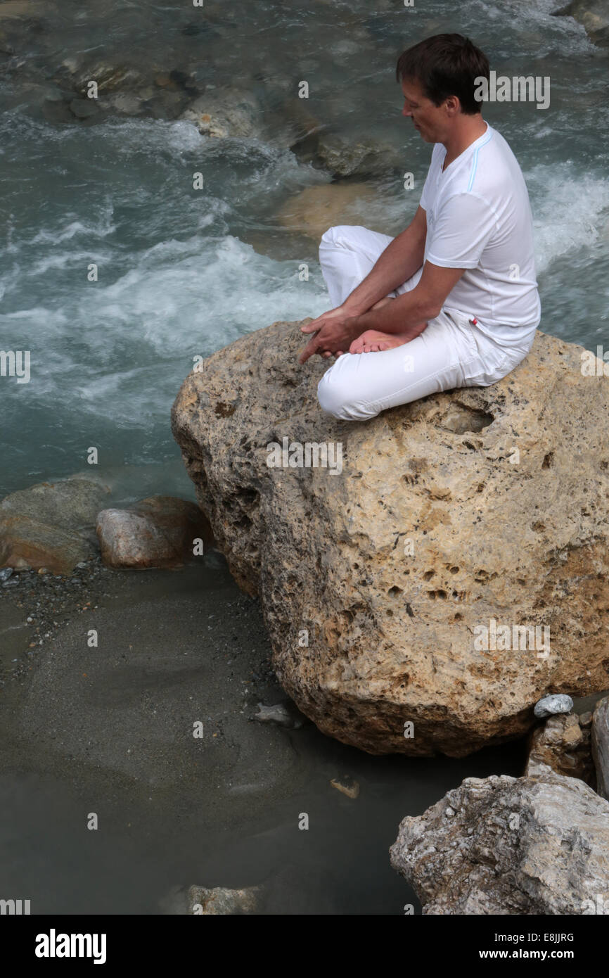 Man meditating on the edge of a stream. Stock Photo