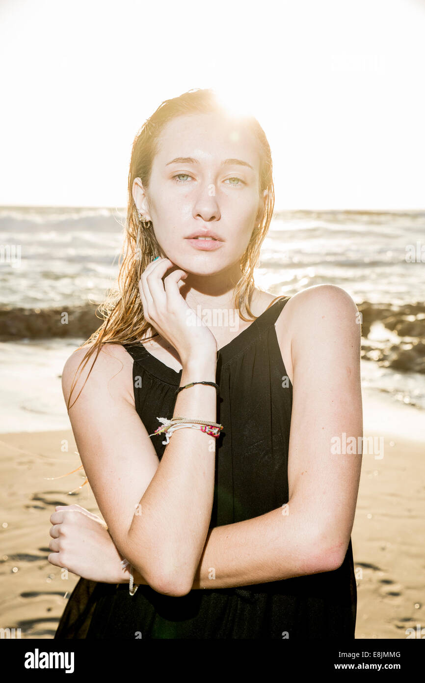 Pensive blond teen in a black dress on a beach. Backlit sun shines on her hair Stock Photo