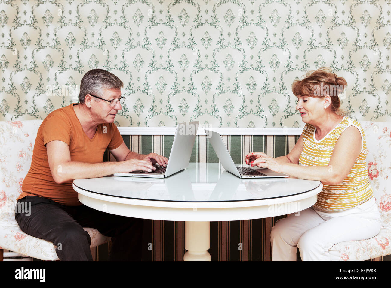 Middle-aged man and mid-adult woman sitting opposite to each other using laptops Stock Photo