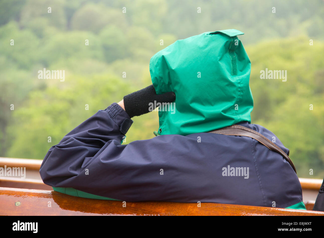 An unidentifiable person wrapped up well against the cold and rain on a Lake Windermere steamer in Spring. Stock Photo