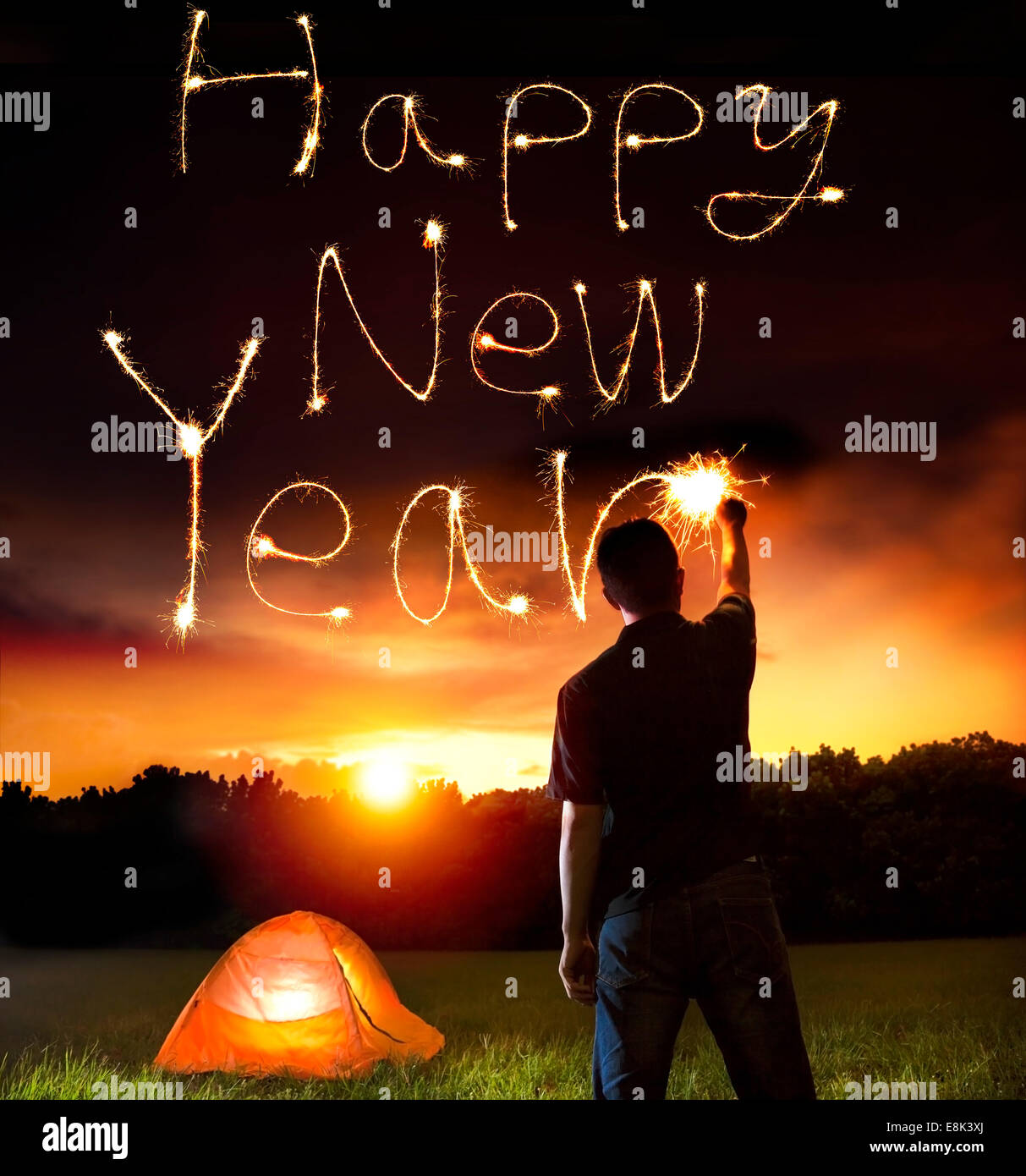 young man drawing happy new year words by sparkling stick. camping on the mountain Stock Photo