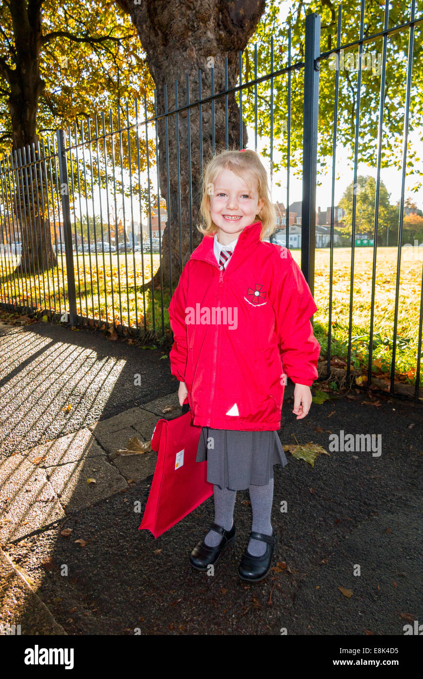 4 Year old child / girl in her new red uniform going to / on the way to her Reception class at State infant primary school. UK. Stock Photo