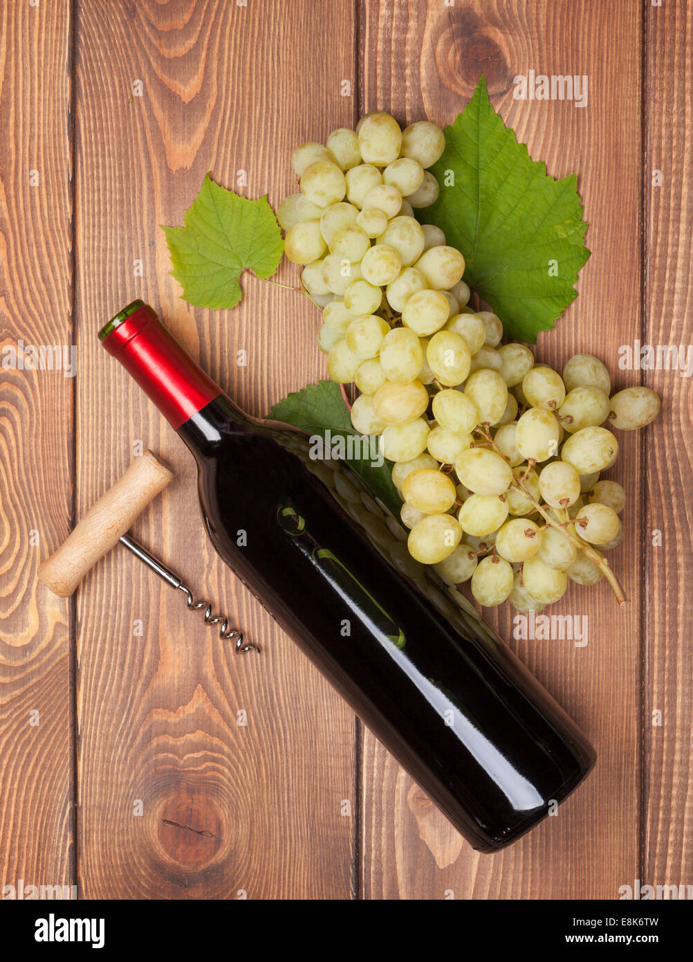 Red wine bottle and bunch of white grapes on wooden table background ...