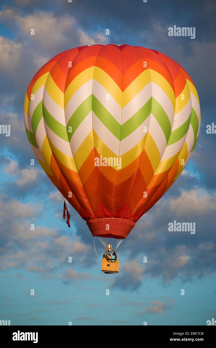 Orange and yellow hot-air balloon floating among clouds Stock Photo