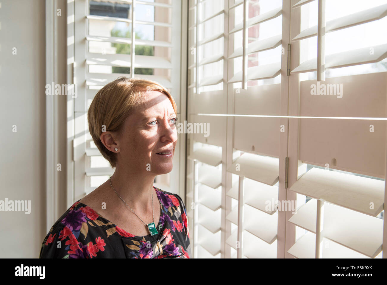 A business woman / mother with short hair stands by Venetian blinds in interesting light Stock Photo