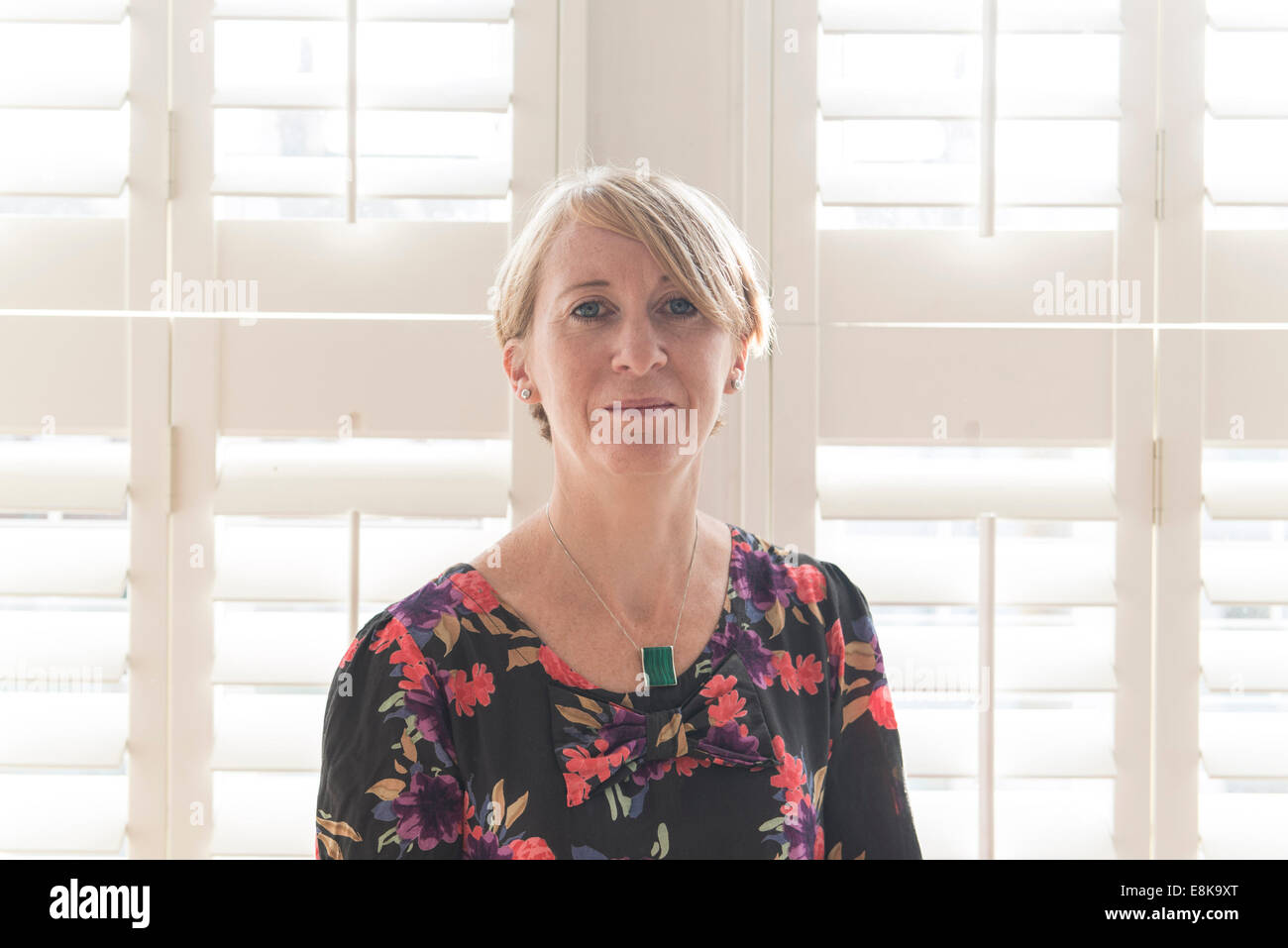 A business woman / mother with short hair stands by Venetian blinds in interesting light Stock Photo