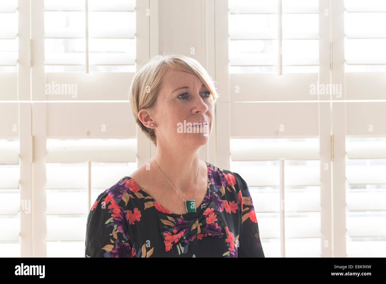 A business woman / mother with short hair stands by Venetian blinds in interesting light Stock Photo