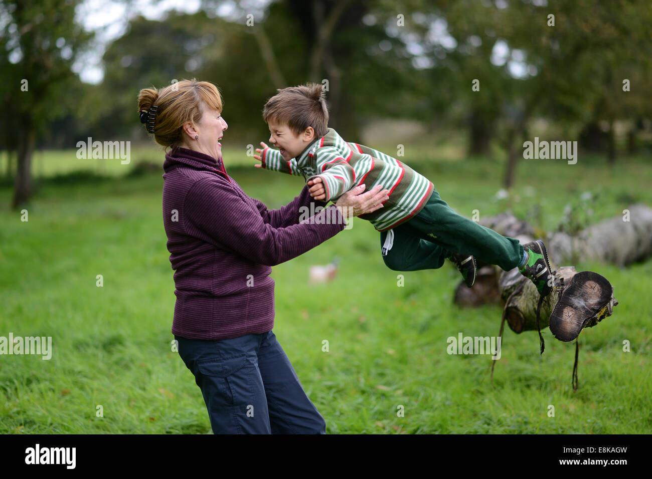 Child children boy having outdoor fun with grandmother jumping into the arms trust trusting Uk Stock Photo