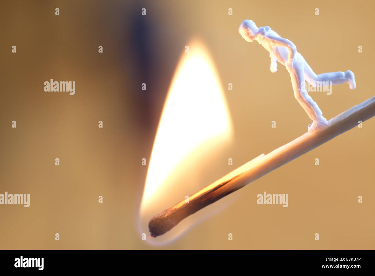 A small figure is running on a burning match towards the flame. Stock Photo