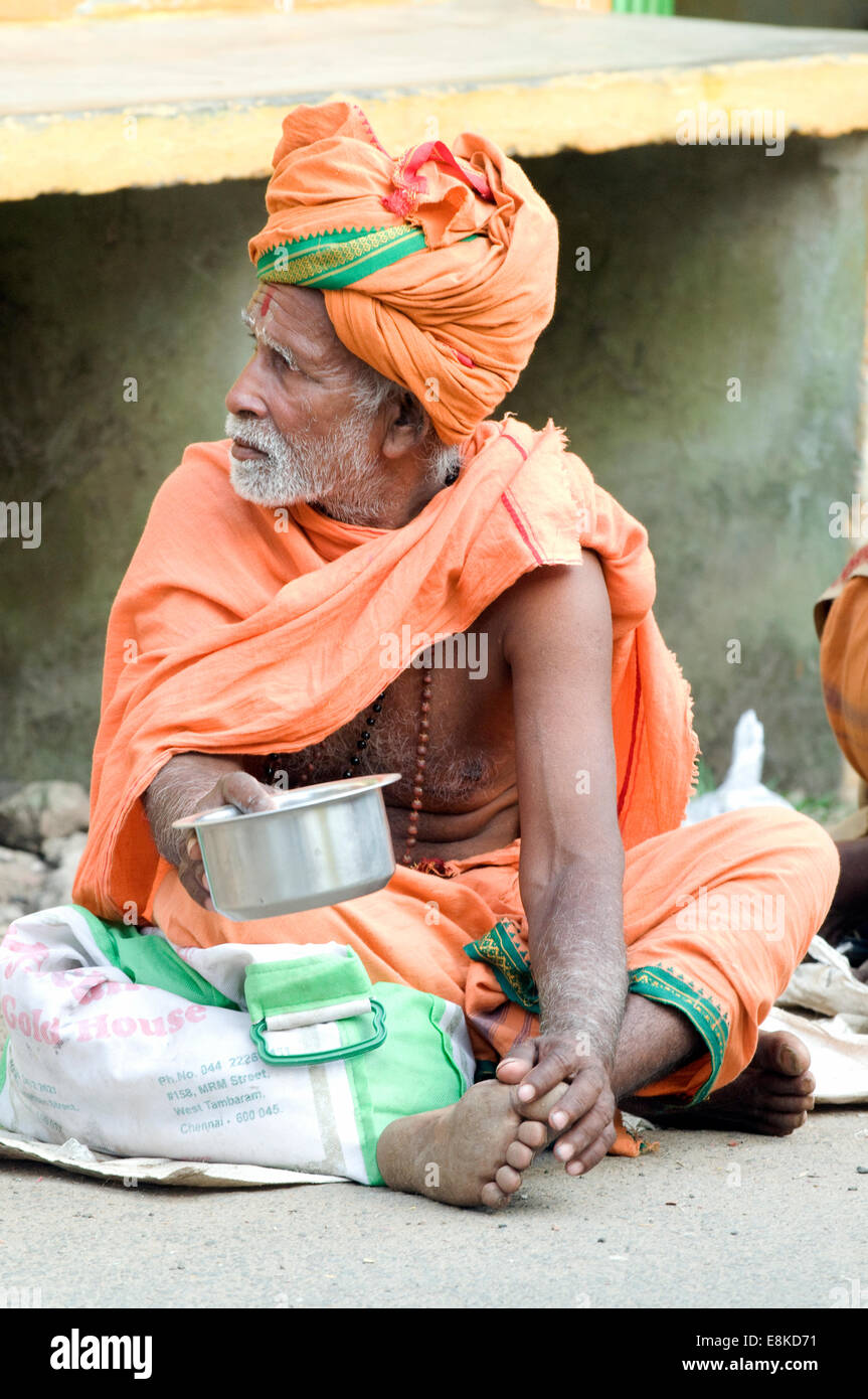 Elegant sadhu sat seeking alms in safron orange turban, shawl & lungi outside Agni (fire) Lingam (Shiva) Pradacshina shrine Stock Photo