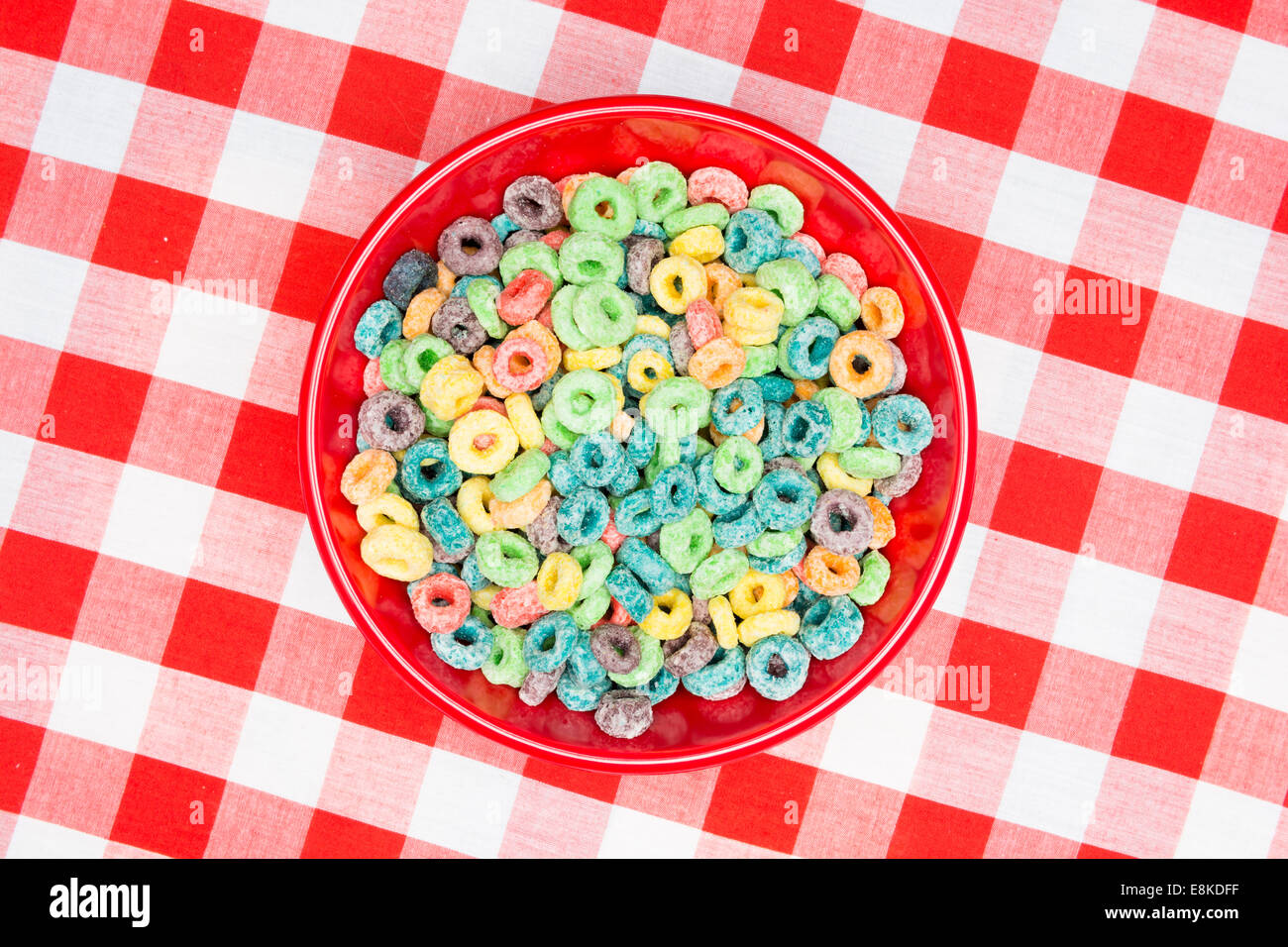 A red bowl of sugary, sweet looped grain cereal and milk on a classic, red, checkered tablecloth ready as a breakfast meal. Stock Photo